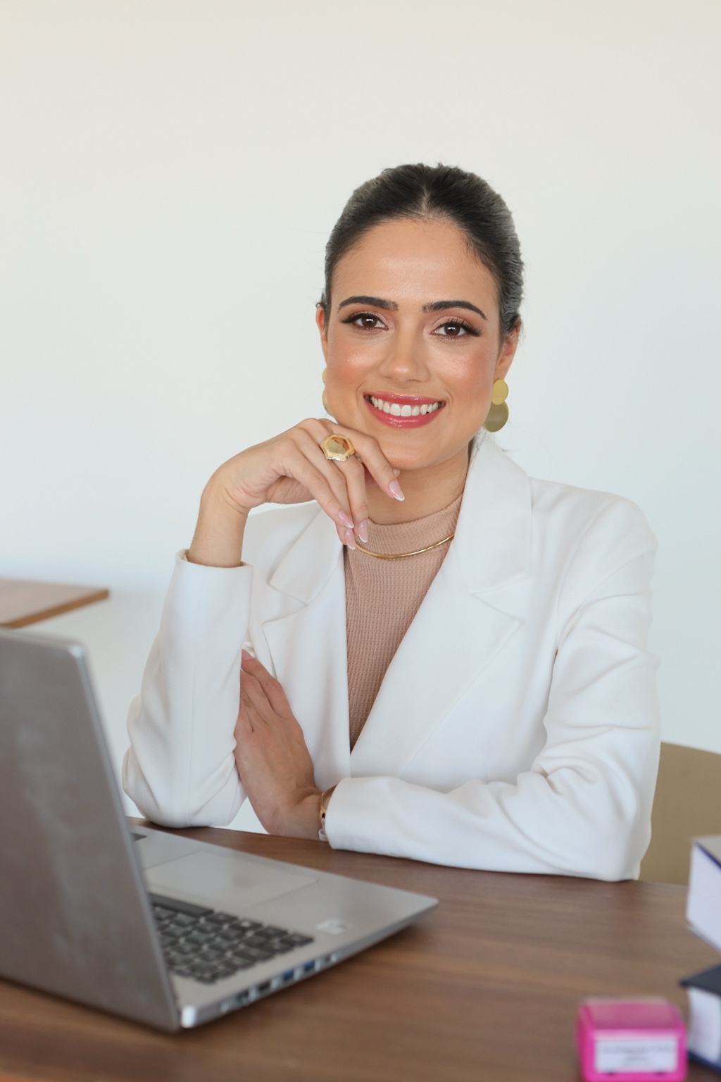 Dra. Ana Beatriz Dias, psiquiatra, sentada à mesa de seu consultório com blazer branco, sorrindo de forma acolhedora.